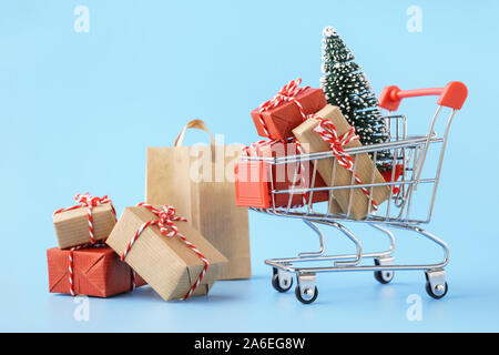 Shopping cart full of various gift boxes and a Christmas tree on light blue background. Christmas sale concept.