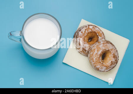 Cup of milk and two cakes on a blue background. Breakfast concept. Cookies on yellow paper napkin. Stock Photo