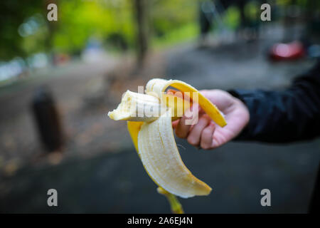 Shallow depth of field (selective focus) image with a woman’s hand holding a half eaten banana Stock Photo