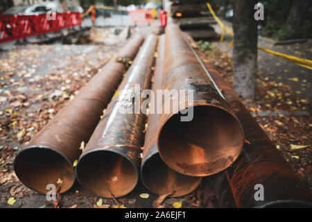 Shallow depth of field (selective focus) image with rusty iron water pipes on the sidewalk with fallen autumn leaves around Stock Photo