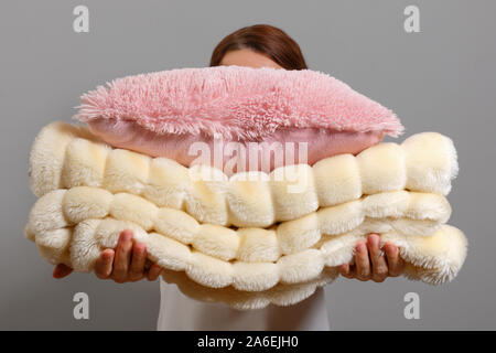 Woman holding a stack of warm fluffy plaid and pillows on a gray wall background. The concept of winter and autumn. Stock Photo