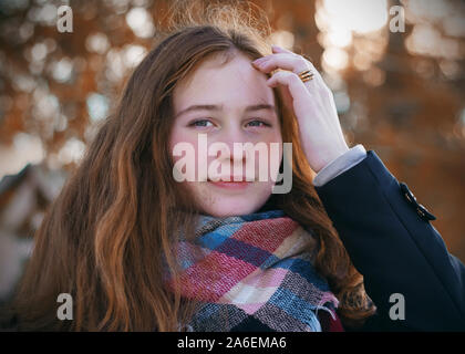 A sweet girl with a satisfied look, red hair, a blush on her cheeks and a happy smile on her face walks on an autumn day, dressed in a dark coat and a Stock Photo