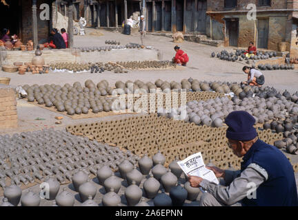 BHAKTAPUR, NEPAL: A Newar man sits reading a newspaper surrounded by traditional clay pottery drying in the sun at Pottery Square. Stock Photo