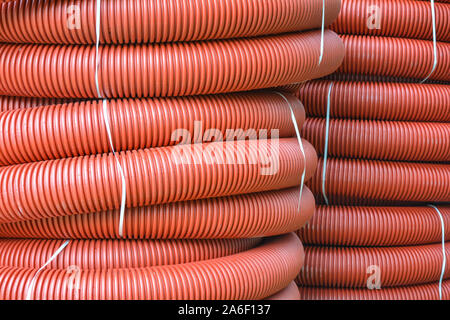 Coils of new red plastic pipe with rain drops. Red plastic tubing for underground cable protection. First floor of a skein of red corrugated tube. Pla Stock Photo