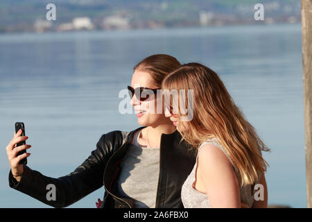 two girls with sunglasses by the lake taking selfies and having fun Stock Photo