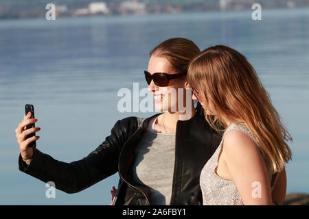 two girls with sunglasses by the lake taking selfies and having fun Stock Photo