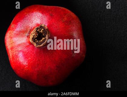 top view of bright, red, whole, fresh pomegranate with black wool felt background Stock Photo