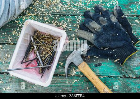 Black textile gloves with hammer chisel and screws on the green wooden bench Stock Photo