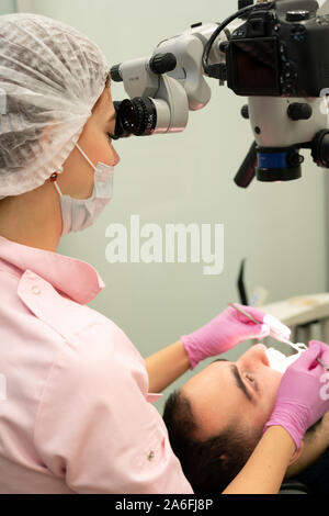 Young female dentist looks through a professional microscope in a dental clinic. Advanced equipment in dentistry. Stock Photo