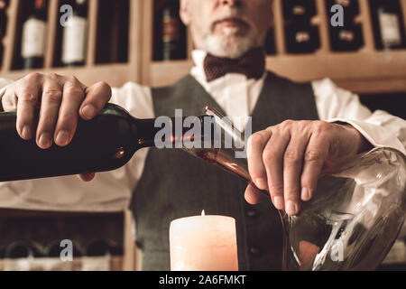 Sommelier Concept. Senior man standing pouring wine into decanter above candle close-up Stock Photo