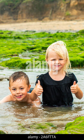 Handsome active little boy with ADHD, Autism, Aspergers Syndrome playing with his sister in the cold algae, seaweed filled water on Walton on the Naze