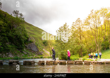 A little boy and girl hoping, jumping over the Dovedale stepping stones across a river, stream in the Peak District National Park, Derbyshire, Autism Stock Photo