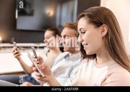 Friends sitting on the couch, smiling, looking at their smartphone, Germany Stock Photo