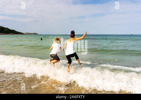 Mother and Daughter spending quality time together, paddling, jumping over waves into sea at the gorgeous St Ives in Cornwall, Carbis Bay Stock Photo
