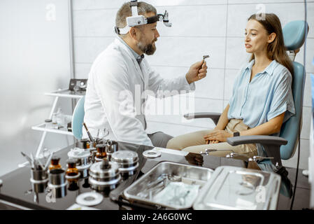 Senior otolaryngologist preparing for the medical examination procedure for a woman patient in the medical office with ENT workstation Stock Photo