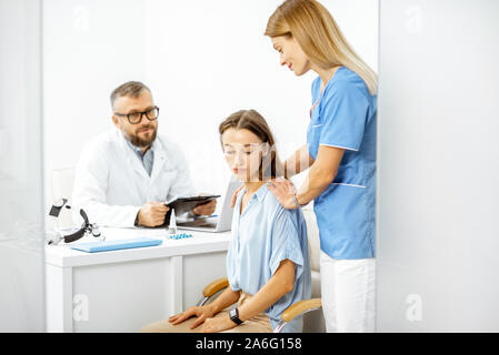 Nurse supporting young patient feeling sad during a medical consultation with senior doctor in the white office Stock Photo