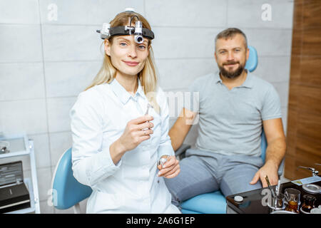 Portrait of a female confident otolaryngologist during a medical examination with adult patient at the ENT office Stock Photo