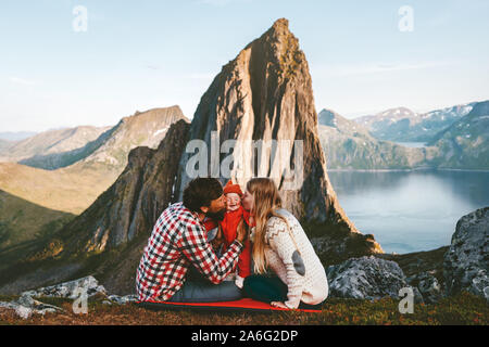 Happy family traveling hiking with baby adventure vacations outdoor mother and father kissing child parenthood lifestyle trip in Norway Stock Photo