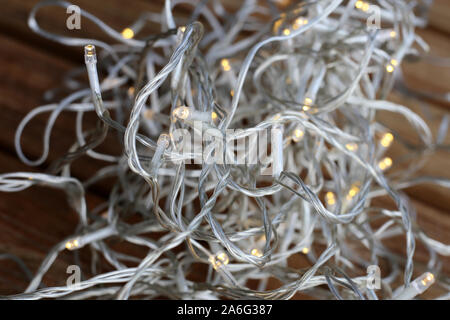 Christmas light string pile on a wooden floor. The string is transparent and the lights are small, light yellow led bulbs. Energy efficient LEDs! Stock Photo