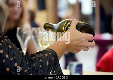 Closeup of a server with Prosecco bottle filling a glass with blurred people in the background Stock Photo