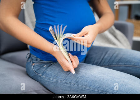 Pregnant Woman Counting US Dollar Bills At Home Stock Photo