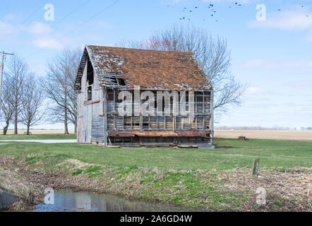 Terrific old and decaying barn with most of one side and part of its roof missing.  Set under blue skies and a green grassy area.  So very picturesque. Stock Photo