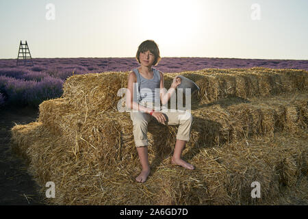 Portrait of a barefoot boy in a sleeveless shirt and trousers with suspenders on a pile of straw. Stock Photo