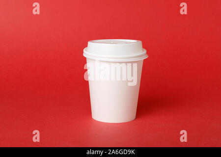 One white disposable paper cup with attached plastic lid on red background. Stock Photo