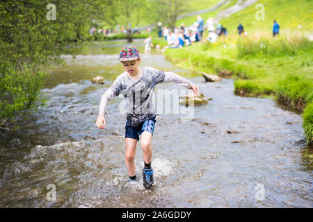 A handsome little boy with ADHD, Autism, Aspergers Syndrome paddles and wades through a cold river, slow flowing river in the Derbyshire Peak District Stock Photo