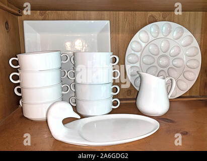 White porcelain dishes including stacks of soup bowls on country hutch's shelf in kitchen. Stock Photo