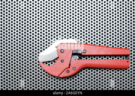 Red scissors for cutting plastic pipe on metal surface Stock Photo