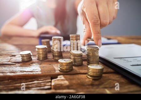 Person Hand Doing Calculation On Stacked Coins At Wooden Desk. Income Tax Concept Stock Photo