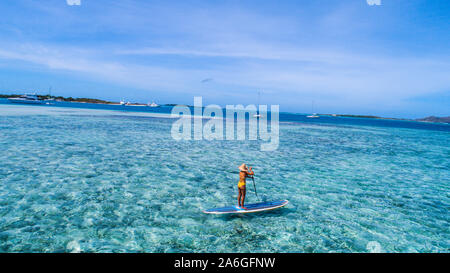 Aerial drone bird's eye view photo of young woman practising paddle board or sup in tropical Caribbean sapphire crystal clear calm waters