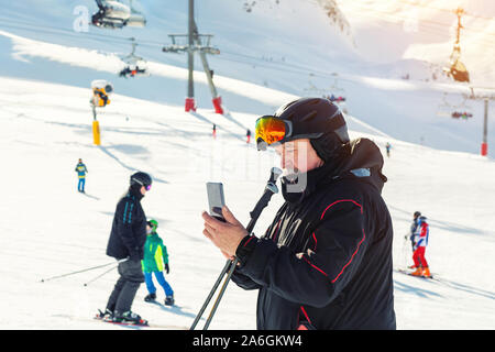 Senior mature skier making selfie with modern camera phone at winter alpine skiing resort. Old aged sporty person using smartphone at mountain Alps Stock Photo
