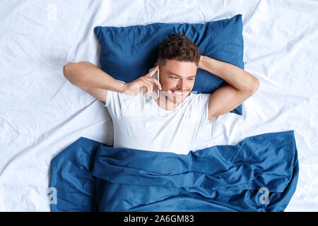 Bedtime. Guy lying on bed top view talking on phone smiling cheerful Stock Photo