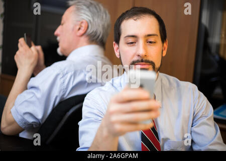 Two lazy businessmen using their phones instead of working Stock Photo