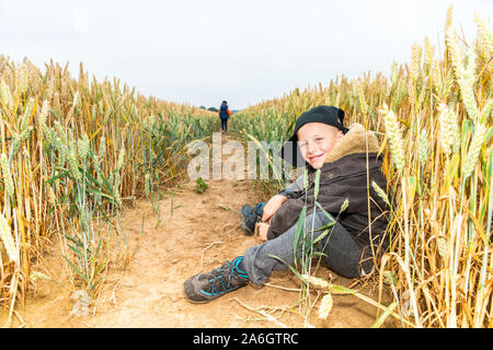 A cheeky little boy sitting in a cornfield wearing a baseball cap, while out playing with friends