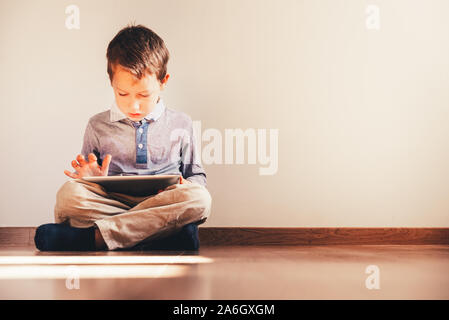 Boy sitting on the floor using a tablet absorbed in it. Stock Photo
