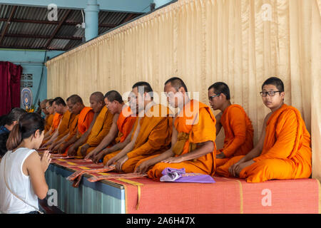 Ko Samui Island, Thailand - March 18, 2019: Wat Khunaram Buddhist Temple and monastery. Devotees kneel in front of  row of praying and chanting monks Stock Photo