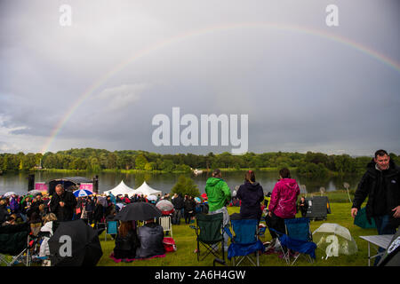 A rainbow in the sky as people cover under umbrella's at an outdoor music festival, raining, Trentham Gardens, main stage Stock Photo