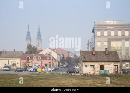 PANCEVO, SERBIA - NOVEMBER 7, 2015: Panorama of Pancevo seen from the city park with an old house in decay in front and the clock towers of the local
