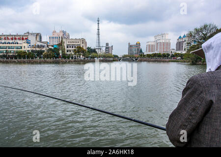 An Asian Chinese man fishing in pond in city. Stock Photo