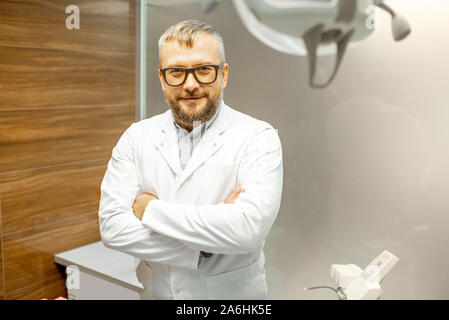 Portrait of a senior male dentist in uniform with eyeglasses standing at the dental office Stock Photo