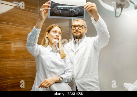 Two experienced dentists examining x-ray of a human jaw at the dental office Stock Photo