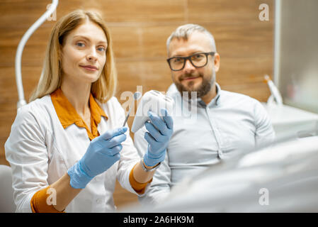 Portrait of a female dentist with tooth model and handsome man as a patient during a medical consultation at the dental office Stock Photo