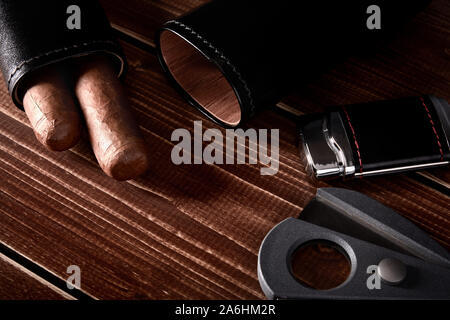 Still life with cuban cigars in black leather case, cutter and lighter on old wooden table top with space for text Stock Photo