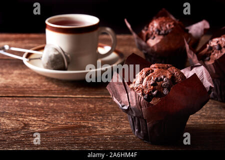 Still life with chocolate muffin and cup of tea on old wooden board table and with black background and space for text Stock Photo