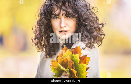 Autumn portrait of young woman with curly hair and bouquet of maple leaves. Stock Photo