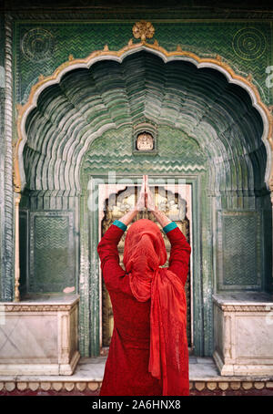 Indian Woman in red scarf with hands in prayer gesture at green gate door in City Palace of Jaipur,  Rajasthan, India. Space for your text, can be use Stock Photo