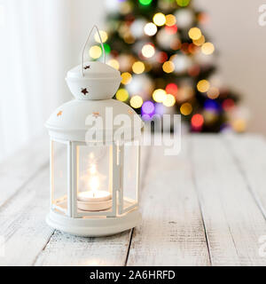 Merry Christmas! White candlestick flashlight stands on the background beautiful blurred christmas tree with luminous garland. Selective focus. Stock Photo